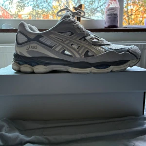 Gråvita Asics sneakers med mesh - Säljer ett par snygga Asics sneakers i grått och vitt med chunky sula och coola detaljer. Ovandelen är i mesh och mocka med klassiska Asics-loggan på sidan. Skorna har snörning och en rund tå, perfekt för dig som gillar sportig stil.