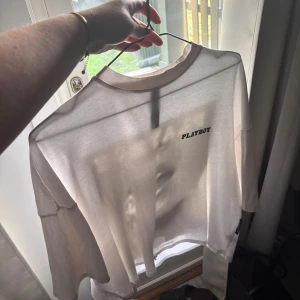 Vit t-shirt  - Säljer en vit t-shirt från Playboy med tryck framtill och ett stort grafiskt motiv på baksidan. Tröjan har en klassisk passform och är gjord i mjuk bomull, perfekt för dig som gillar streetstyle och statement-plagg.