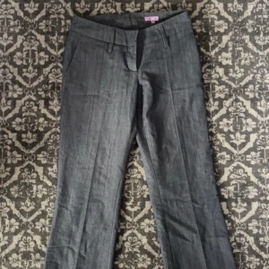 Grå kostymbyxor låg midjade - Låg midjade snygga grå kostymbyxor med raka ben och pressveck. Byxorna har hällor för bälte, sidfickor fram och knäppning med dragkedja. Baktill finns två fickor med knapp. Perfekta för en clean och stilren look.