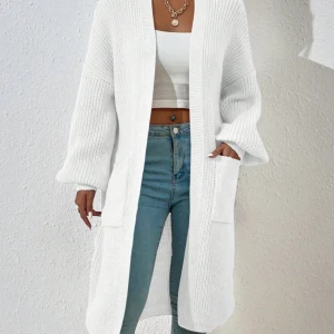 Vit lång stickad kofta  - Säljer en vit lång stickad kofta med oversized passform och stora fickor framtill. Koftan har ribbade muddar och är perfekt att slänga över en topp för en chill och snygg look. Passar både till jeans och mjukisbyxor.