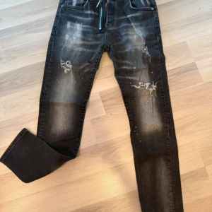 Svarta skinny jeans med slitningar - Säljer ett par svarta dsq2 jeans med skinny passform och coola slitningar samt blekta detaljer på både fram- och baksida. Jeansen har klassisk femficksdesign, dragkedja och knappstängning. Perfekt för dig som gillar en edgy streetstil.