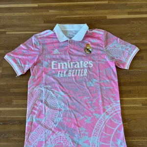 Real Madrid rosa fotbollströja Adidas - Supersnygg rosa Real Madrid-tröja från Adidas med klubbemblem på bröstet och klassisk design i lätt ClimaCool-material som andas. Perfekt både till träning och streetwear!  ✔️ Lätt och snabbtorkande tyg ✔️ Korta ärmar, regular fit ✔️ I mycket fint skick  Passar dig som gillar fotboll, sportmode eller unika matchtröjor. Storlek: M Skick: Utmärkt (aldrig andvänd) 