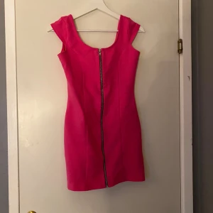 Rosa kort klänning med dragkedja - Snygg rosa kortklänning med markerad midja och breda axelband. Klänningen har en cool dragkedja framtill som ger en edgy vibe. Tillverkad i ett mjukt bomullstyg som sitter skönt och följer kroppen. Perfekt för dig som vill sticka ut med färg och enkel design.Frakt ingår inte 