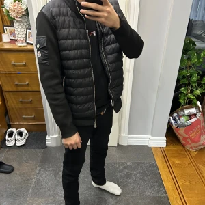 Svart dunväst från Moncler - Säljer en svart gammal model Moncler jacka som jag fått av min storebror. Denna gamla modellen har ingen qc på Moncler loggan vid armen eftersom det är en gammal model.
