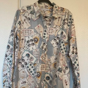 Mönstrad skjorta från & Other Stories - skjorta från & Other Stories i 100% bomull med coolt kortleksinspirerat mönster i vitt, beige, blått och svarta detaljer. Skjortan har klassisk krage, knäppning framtill och långa ärmar. 