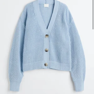 Ljusblå stickad kofta från H&M - Superfin ljusblå stickad kofta från H&M med stora bruna knappar framtill. Koftan har v-ringning, ribbade muddar och en loose passform som ger en chill vibe. Perfekt att slänga på sig över en t-shirt eller linne.
