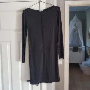 Svart långärmad klänning Filippa K XS - En stilren svart klänning från Filippa K i storlek XS. Modellen är kort med lång ärm och har en rak, enkel siluett med diskret söm framtill. Materialet är mjukt och stretchigt, vilket gör den bekväm och lätt att bära.