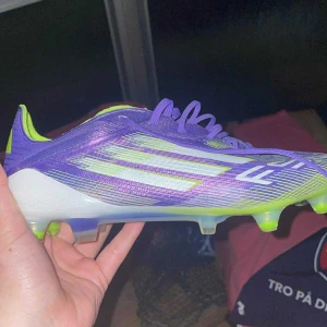 Adidas F50 lila fotbollsskor - Säljer ett par Adidas F50 fotbollsskor i lila och neongult med vita detaljer. Skorna har snörning, platt sula med utbytbara dobbar och är tillverkade i syntetmaterial. Perfekta för dig som vill sticka ut på planen och få grymt grepp på gräs och konstgräs dobbar följer i packet. Kan trade mot puma future senaste modellen eller predators röda 