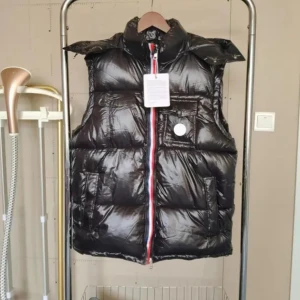 Svart dunväst från Moncler - Glansig svart dunväst från Moncler med hög krage och breda kanaler. Västen har en röd, vit och blå randig dragkedja framtill, bröstficka med knapp och två sidofickor. Perfekt för lager-på-lager under kyliga dagar.