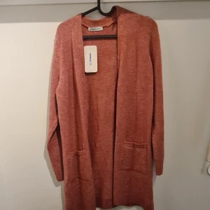 Rosa kofta från LC Waikiki Basic - Lång, stickad kofta i en mjuk rosa nyans från LC Waikiki Basic. Koftan har två fickor framtill, öppen front och långa ärmar. Perfekt för lager-på-lager och chill dagar. Enkel och stilren design som funkar till det mesta.