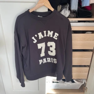 Svart sweatshirt med tryck 'J'AIME PARIS 73' - Cool svart sweatshirt med vitt tryck 'J'AIME PARIS 73' på bröstet. Tröjan har rund halsringning och långa ärmar, perfekt för en avslappnad och trendig look.