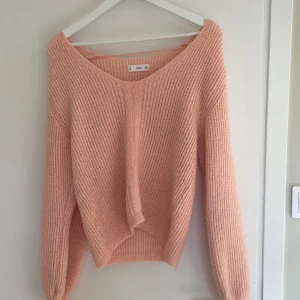 Ljusrosa stickad tröja från Mango - Supermjuk och mysig ljusrosa stickad tröja från Mango med v-ringad hals och långärmad design. Tröjan har en avslappnad passform och ribbade detaljer längs ärmslut och nederkant. Perfekt för lager-på-lager under kyliga dagar.