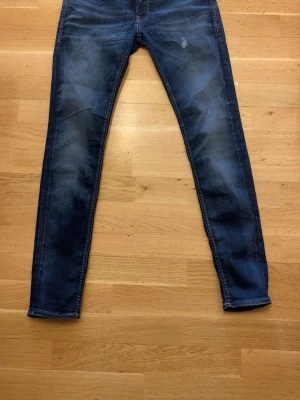 Mörkblå skinny jeans från Jack & Jones - Snygga mörkblå skinny jeans från Jack & Jones med klassisk femficksdesign och diskreta slitningar framtill. Jeansen har en smal passform och är tillverkade i stretchigt denim för extra komfort. Perfekta för dig som gillar en modern och stilren look.