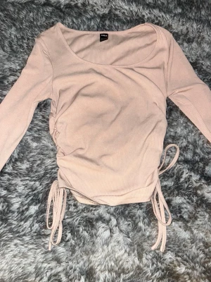 Beige omlottopp med snörning från SHEIN - Trendig beige omlottopp från SHEIN med långa ärmar och snygg snörning i sidorna. Toppen är ribbad och har en figurnära passform som framhäver siluetten. Perfekt att styla med jeans eller kjol för en cool look.