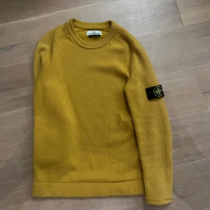 Stone Island tröja - Säljer en äkta och snygg gul stickad tröja från Stone Island med klassisk rund hals och soprena linjer. De är storlek Small men sitter som S/M. Tröjan har en ikoniska patchen på vänster ärm och är tillverkad i mjukt material som känns skönt mot huden. Perfekt för dig som vill ha en stilren och trendig look.
