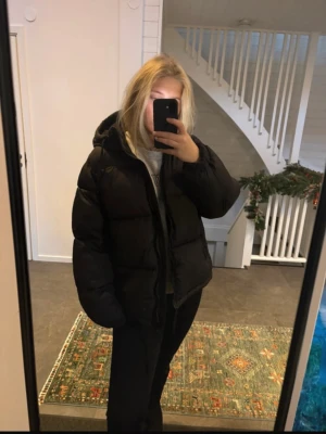 Svart pufferjacka med huva - Säljer en svart pufferjacka med huva och dragkedja. Jackan är oversized och har en riktigt fluffig look som håller dig varm under kalla dagar. Perfekt för dig som gillar en chill och trendig stil. Jackan har långa ärmar och dragsko nertill för extra komfort.