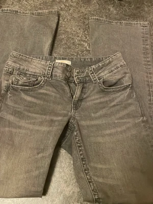 Grå bootcut jeans med låg midja - Snygga grå jeans med bootcut-modell och låg midja. Jeansen har klassiska fem fickor och stängs med dragkedja och dubbla knappar. Perfekta för dig som gillar en avslappnad och trendig stil.