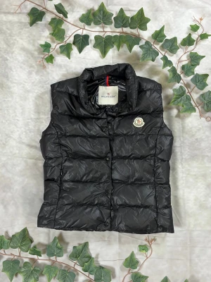 Moncler Ghana Down Vest – Svart – Strl 1 - |Färg: Svart, blank nylon | Modell: Ghana Down Vest, quiltad | Storlek: 1 (XS/S), smal/normal passform | Skick: Grade A, 9,5/10 | Hör av dig ifall du har funderingar!