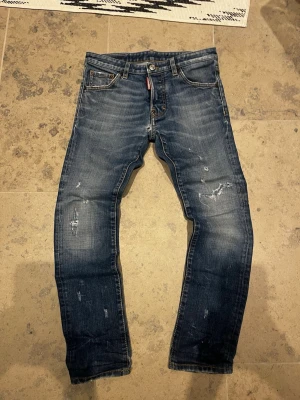 Blå jeans från Dsquared2 med slitningar - Snygga blå jeans från Dsquared2 med slitna detaljer och broderad bakficka. Jeansen har normal passform, klassisk femficksdesign och knappgylf. Perfekta för dig som gillar en avslappnad men trendig stil.