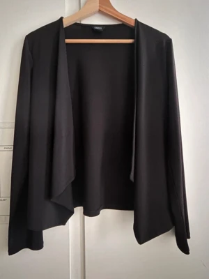 Svart öppen cardigan från Lindex - Stilren och lättmatchad svart cardigan från Lindex. Modellen är öppen framtill och faller snyggt med ett fint, draperat uttryck. Perfekt både till vardag och jobb, eller som ett lätt lager över en topp eller klänning.  Skick: Som ny – använd bara ett fåtal gånger. Färg: Svart Storlek: S Passform: Lätt och ledig, utan knäppning  En tidlös basplagg som är superlätt att styla och passar året runt!