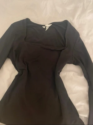 Svart långärmad topp med fyrkantig ringning - Snygg svart långärmad topp med en modern fyrkantig ringning. Toppen har en tight passform och är tillverkad i ett mjukt bomullsliknande material. Perfekt att styla med jeans eller kjol för en trendig look. Den är från H&M och bara använd en gång. Storlek S