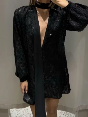 Svart glittrig kortklänning -  en svart glittrig kortklänning med lång ärm och djup v-ringning. 