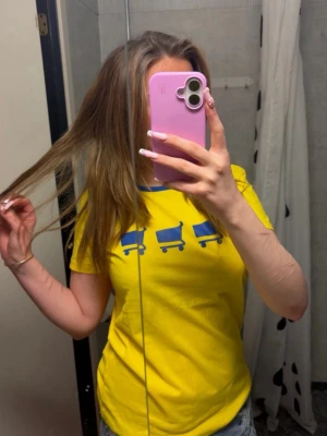 Gul t-shirt med blå kundvagnar - Cool gul t-shirt med blå tryck av tre kundvagnar på bröstet och blå kant vid halsen. Perfekt för dig som gillar färgglada och unika plagg. Skön passform och passar till jeans eller shorts.