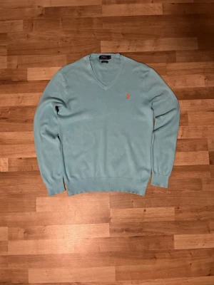 Vintage Polo Ralph Lauren Knit V-Neck – Turquoise – Orange/Red Logo – Size M – Unisex - Vintage knitted Polo Ralph Lauren V-neck pullover in a beautiful turquoise color. Features the iconic Polo Ralph Lauren horse logo embroidered in orange/red on the chest, giving the sweater a nice contrast and classic look. The sweater has been lightly used. There are small minor stains, but they are hardly noticeable and do not affect the overall appearance. Otherwise in very nice condition.• Brand: Polo Ralph Lauren • Size: M • Color: Turquoise• Condition: Very good vintage condition – lightly