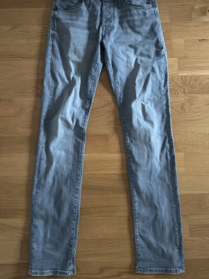 Grå slim jeans från Jack & Jones - Snygga grå slim fit jeans från Jack & Jones, modell Glenn. Klassisk femficksdesign och normal midja. Jeansen är tillverkade i mjuk bomullsdenim med lite stretch för extra komfort. Perfekta till en avslappnad och stilren look.