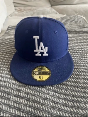Blå LA Dodgers keps New Era 59FIFTY - Pris kan diskuteras vid snabb affär. Knappt använd, Snygg blå LA Dodgers keps från New Era 59FIFTY-serien med broderad vit LA-logga framtill och MLB-logga bak. Klassisk flat peak och strukturerad passform. Perfekt för dig som gillar sportig streetstyle.
