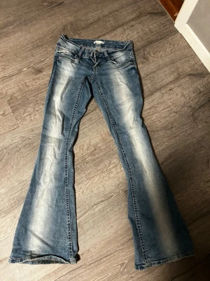 Blå bootcut jeans från Gina Tricot - Ett par blåa jeans med ljusare på visst ställe på benen och även där bak. Är från Gina 14+ i storlek S. De är även lågmidjade.