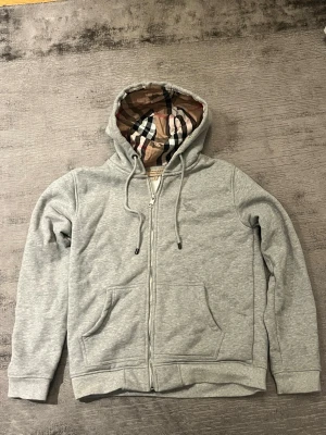 Burberry Zip - En burberry zip i helt nytt skick använd 2-3 gånger. Den är i storlek M men för mig som är 186 så är den lite för liten, skulle säga att den passar dig som är mellan 175-184.             Säljer åt en vän skriv vid några funderingar