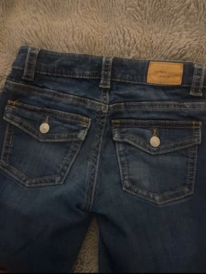 Blå bootcut jeans med fickdetaljer - Säljer mina jeans eftersom de tyvärr blivit för korta för mig (är 165 cm). De skulle passa perfekt pả năgon som är cirka 150-160 cm. Jeansen är i fint skick och har använts sparsamt. De sitter bra och är bekväma, och färgen samt materialet ar fortfarande som nya.💗