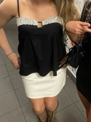 Svart topp med strassdetaljer - Säljer en svart linnetopp med tunna axelband och glittriga strassdetaljer längs bysten. Toppen har en lös passform och ett litet nyckelhålsutskärning framtill. Perfekt för dig som vill sticka ut lite extra.