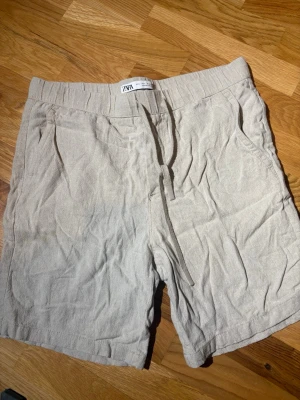 Beiga linneshorts från Zara - Snygga beiga shorts från Zara i luftig linnemix. De har elastisk midja med snörning och två sidofickor. Perfekta för varma dagar och enkel att matcha med t-shirt eller skjorta.