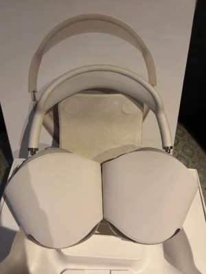 Vita Apple AirPods Max over-ear hörlurar - Snygga vita Apple AirPods Max over-ear hörlurar med stilren design. Tillverkade i aluminium och mjukt mesh-tyg för extra komfort. De har en bred, vadderad bygel och stora öronkuddar som omsluter öronen helt. Perfekta för musik, film och gaming.