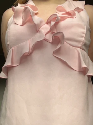 Ljusrosa blus med volangdetaljer - Supersöt ljusrosa blus från missäy med volanger längs ringningen och framtill. Ärmlös modell i ett lätt och mjukt tyg, perfekt till våren 💐