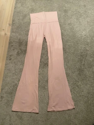 Ljusrosa yoga pants - Snygga ljusrosa yoga pants med nervikbar midja och utsvängda ben. Mjukt och stretchigt material som sitter skönt på kroppen. Perfekta för dig som gillar en trendig och bekväm stil.