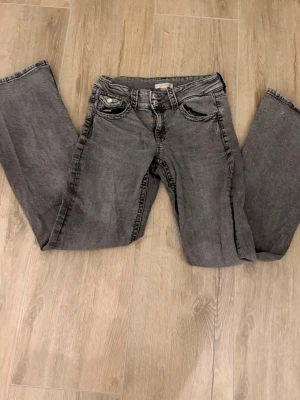 Grå jeans från Gina Tricot med låg midja  - Säljer ett par grå jeans från Gina Tricot i bootcut, låga i midjan och dubbla knappar i midjan. Klassisk femficksmodell i mjukt bomullsmaterial. Perfekta till en avslappnad look och passar till det mesta. Jeansen är i barn storlek 170 men skulle säga att de blir ungefär en S. 