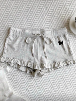 Gråa loungewear shorts med volang - Supermjuka grå shorts med volangkant och söt svart kattdetalj framtill. Säljer på grund av att de var för små💓Perfekta för chill hemma eller mysiga kvällar. 