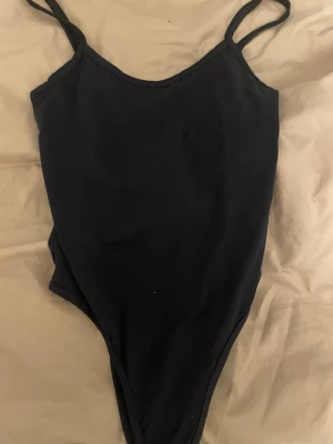 Mörkblå basic body med smala axelband - En enkel och stilren mörkblå body med smala axelband och rundad uringning. Materialet känns mjukt och stretchigt för skön passform.