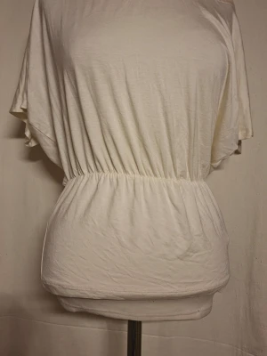 Ljusgul topp med knyt och resårmidja och slitz baktill - Snygg ljusgul topp från object med lös passform, resår i midjan och korta ärmar. Toppen har knyt i nacken och dekorativt band längs halsringningen plus slitz baktill. Perfekt för en avslappnad och trendig look.