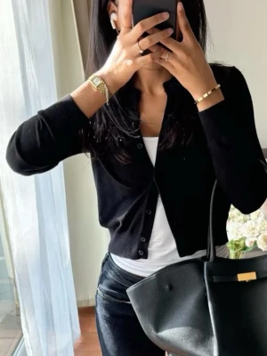 Svart kofta med knappar - Stilren svart kofta med knappar framtill och lång ärm. Klassisk passform och enkel design som passar till det mesta. Perfekt att slänga över en topp eller t-shirt för en snygg lager-på-lager-look.