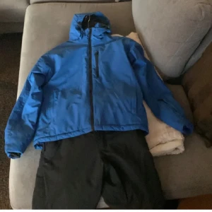 Blå skidjacka - Blå skidjacka med huva. Använd två säsonger i fjällen men ändå i bra skick. Perfekt för kyliga dagar på fjället. Säljer även ett par byxor om man vill ha hela kitet.