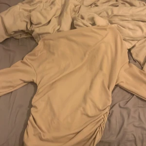 Beige ribbad kortklänning med rynk - Supersnygg beige tröja med långa ärmar och ribbad struktur. Tröjan har en cool rynkdetalj på sidan som ger en trendig look. Perfekt för dig som gillar stilrena plagg med en twist. Materialet känns mjukt och följsamt. Jätte skön tröja om jag får säga det själv.