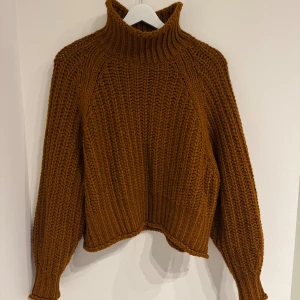 Brun stickad polotröja från H&M - Säljer en chunky brun stickad polotröja från H&M i storlek S. Tröjan har hög krage, grov ribbstickning och långa ärmar med breda muddar. Perfekt för dig som gillar en cozy och trendig look under kyliga dagar.
