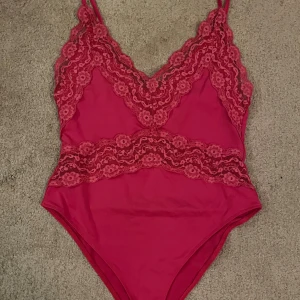 Rosa spetsbody från Zara - Säljer en snygg rosa body från Zara i storlek M. Bodyn har tunna axelband och är dekorerad med blommig spets upptill och runt midjan. Materialet är mjukt och stretchigt, perfekt för att skapa en cool och feminin look. Spetsdetaljerna ger en extra touch.