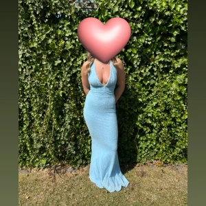 Ljusblå glittrig långklänning - Supersnygg ljusblå långklänning med glittrigt tyg och djup v-ringning. Klänningen är figurnära, har öppen rygg och är ärmlös. Perfekt för bal eller student! Materialet är stretchigt och skimrar fint i ljuset.