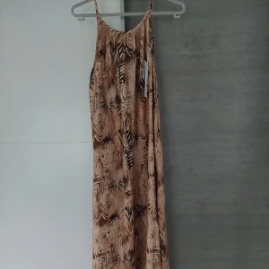 Suncoo långklänning sandmönstrad - Suncoo kläning med tunna axelband i ett sandfärgat och brunt abstrakt mönster. Lätt och flowy passform, perfekt för varma dagar. Färgerna går i beige, brun och grå toner. Klänningen har en avslappnad siluett och är ärmlös. Nypris 1699kr säljes för endast 550kr ett kap stl 40 passar från 34 till en 40 