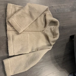 Beige teddyjacka med dragkedja - Säljer en beige teddyjacka från H&M i storlek M. Jackan har en oversized passform, två stora fickor framtill och en rejäl krage. Materialet är mjuk fleece som känns riktigt cozy. Perfekt för kyliga dagar och enkel att matcha med jeans eller hoodies.